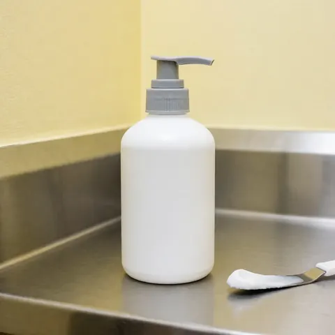 Grey pump bottle of foot cream with a spoonful of cream beside it on a clean stainless steel surface in a professional setting