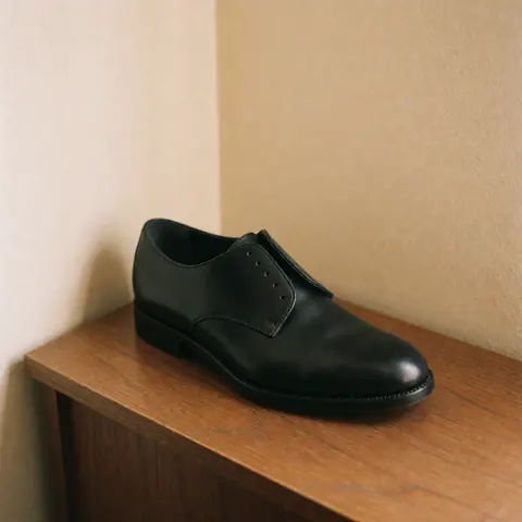 A detailed view of a restored black leather shoe resting on a beige wooden surface, highlighting the texture and craftsmanship of the footwear.
