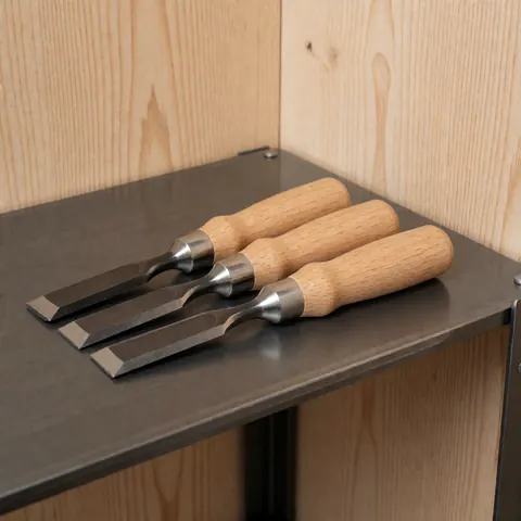 Three chisels with light wood handles and metal ferrules arranged neatly on a dark metal surface with a light wood background.