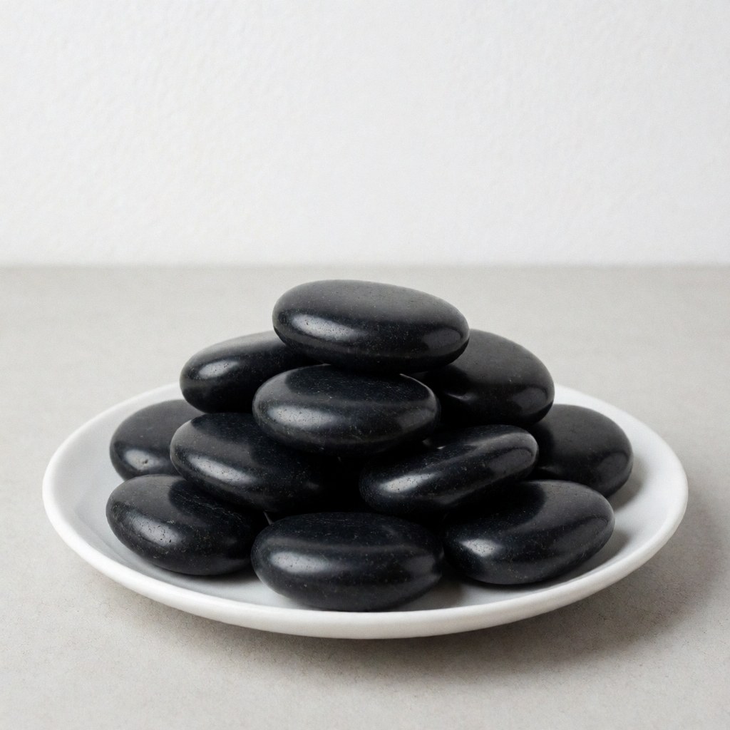Polished black basalt stones arranged on a white ceramic plate against a neutral gray background with soft lighting