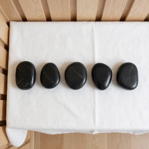 Five smooth, shiny black hot stones arranged on a white cloth over a light wood background, ideal for spa and massage services.