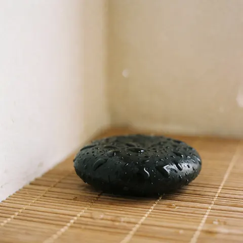 Detailed view of smooth black basalt stones used in hot stone massage therapy, emitting gentle steam for relaxation and wellness.