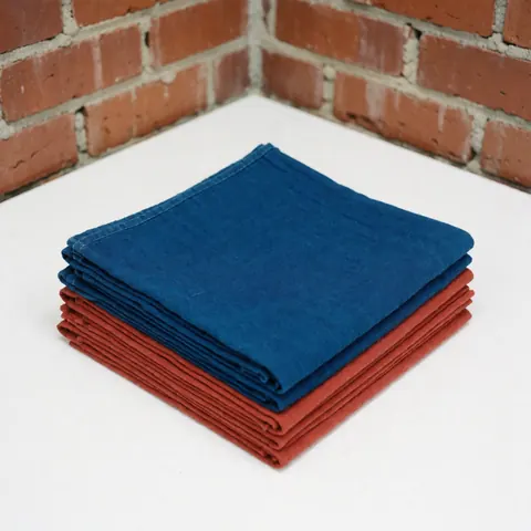 Close-up view of dyed cotton fabric samples in indigo and terracotta colors displayed against a rustic brick wall for product presentation