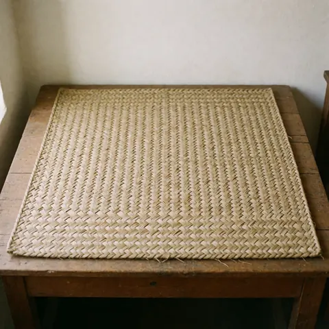 Close-up of a handcrafted woven palm fiber rug placed on a rustic wooden table surface with natural lighting