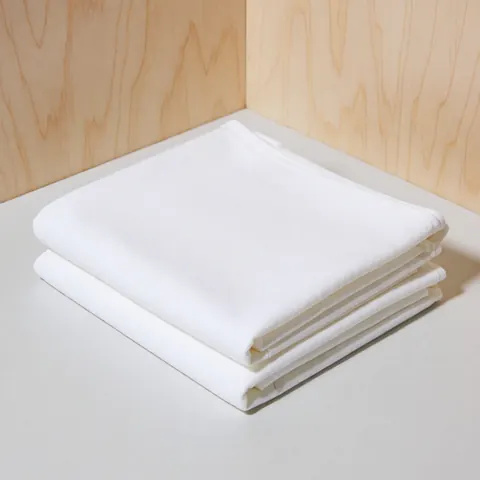 Close-up of a soft white cotton textile draped over a wooden surface, showcasing its texture and weave for product display