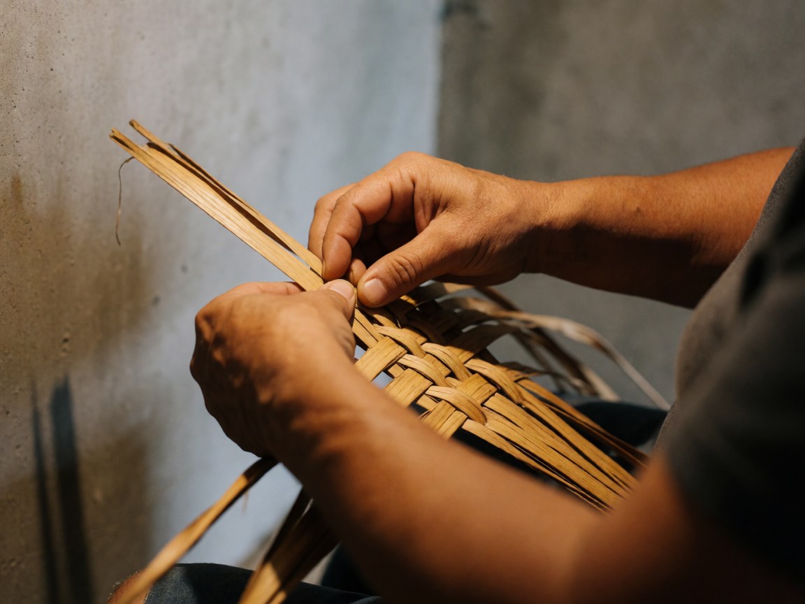Close-up of artisan hands weaving dry palm fibers with precision against a concrete wall, highlighting texture and traditional craftsmanship.