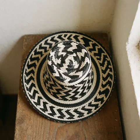 A traditional black and white woven Vueltiao hat resting on a rustic wooden bench against a white wall with natural light