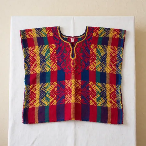 Close-up view of a traditional Guatemalan huipil featuring vibrant geometric patterns and intricate weaving details on a white background