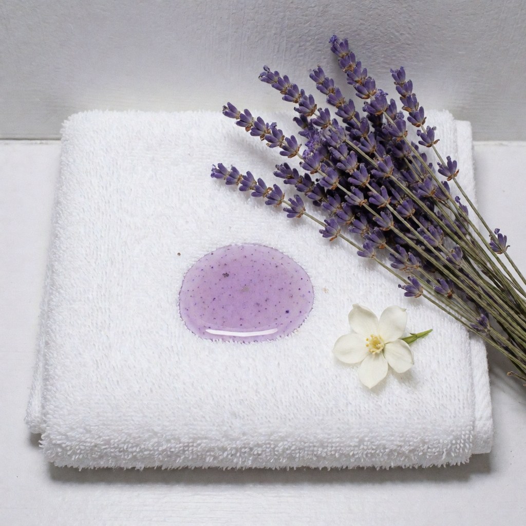 Folded white towel with lavender jasmine oil, dried lavender sprigs, and a white jasmine flower on a light gray background for spa and massage use