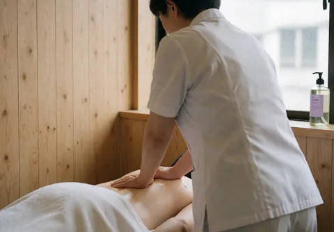 Therapist performing Swedish massage in a spa room with wooden walls, client in white clothing, natural light from window, relaxing and professional atmosphere.