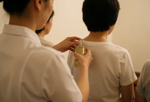 A therapist applies massage oil to a client's back in a calm spa setting with warm lighting and white uniforms.