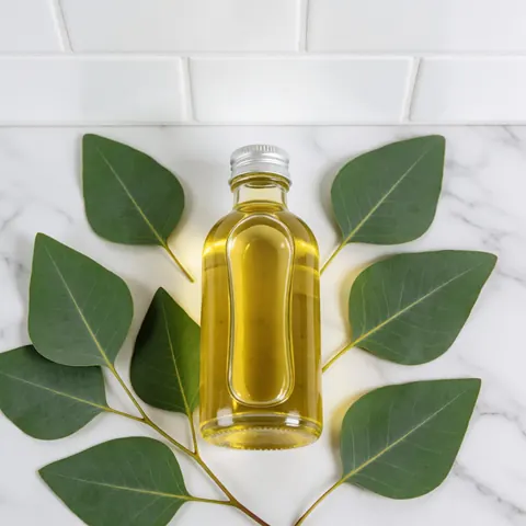 A clear glass bottle filled with eucalyptus oil placed on a white marble surface for massage and spa treatments