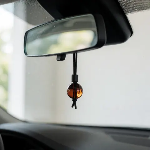A spherical car air freshener hanging by a black chain from the rearview mirror inside a vehicle, designed to release a relaxing aroma and improve the interior ambiance.