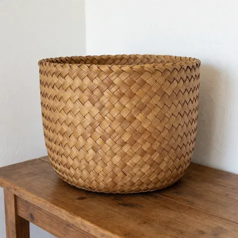 A round woven palm basket placed on a rustic wooden table against a white wall, showcasing natural texture and organic materials for home decor.