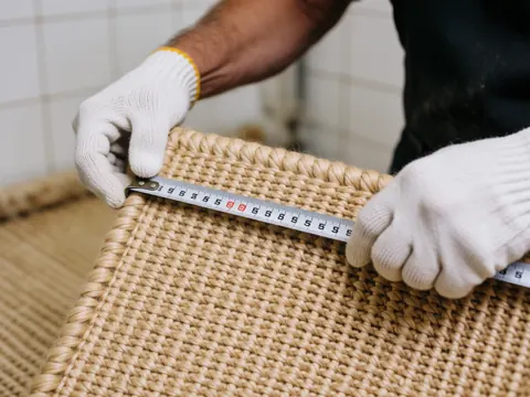 Close-up of a hand using a metal ruler to measure the dimensions of a woven carpet, highlighting the textile texture and craftsmanship details.