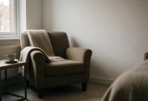 A comfortable rest chair with a blanket and cup near a window, creating a relaxed atmosphere for reflexology.