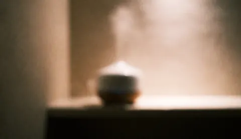 Soft focus background featuring an essential oil diffuser emitting steam, creating a relaxing spa atmosphere with warm lighting and blurred bokeh effects suitable for text overlay