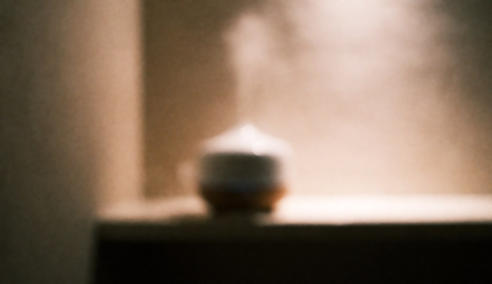 Soft focus background featuring an essential oil diffuser emitting steam, creating a relaxing spa atmosphere with warm lighting and blurred bokeh effects suitable for text overlay