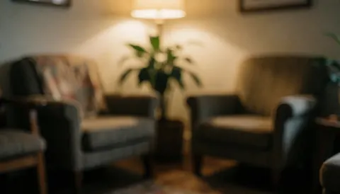 A cozy waiting room interior featuring comfortable armchairs, a potted plant, and warm ambient lighting, creating a calm atmosphere suitable for text overlay
