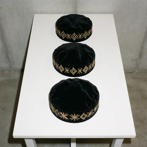 Three black velvet hats featuring gold embroidery arranged in a row on a white table, ideal for showcasing custom apparel products.