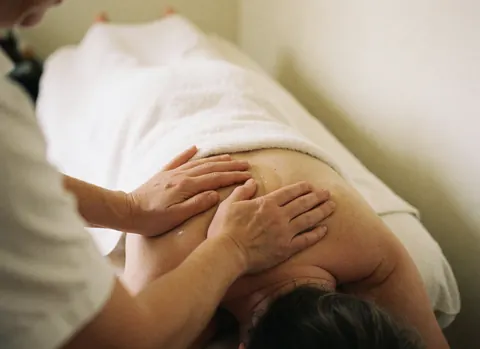 Close-up of therapist hands massaging a client's shoulder with oil against a soft white background for a relaxing atmosphere