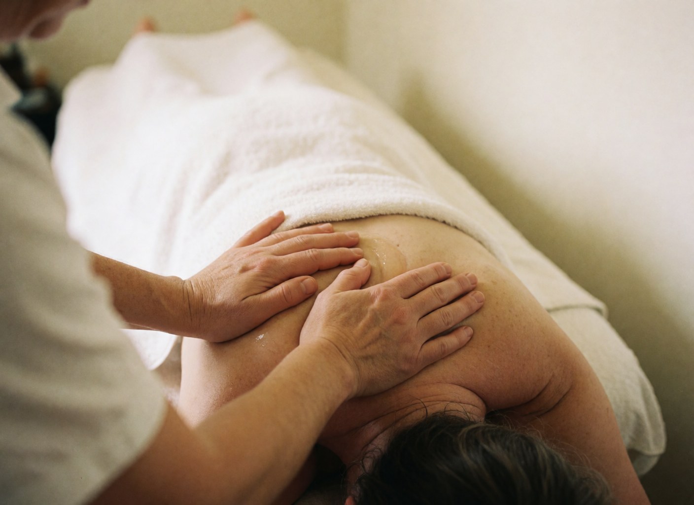 Close-up of therapist hands massaging a client's shoulder with oil against a soft white background for a relaxing atmosphere