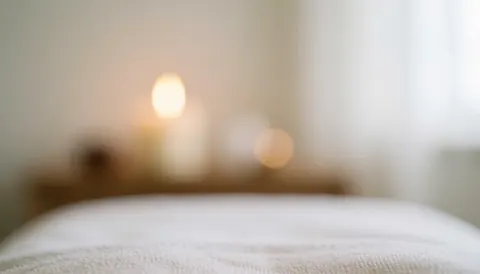 White massage bed with a lit candle, soft lighting, and bokeh effect, ideal for relaxation and wellness text backgrounds