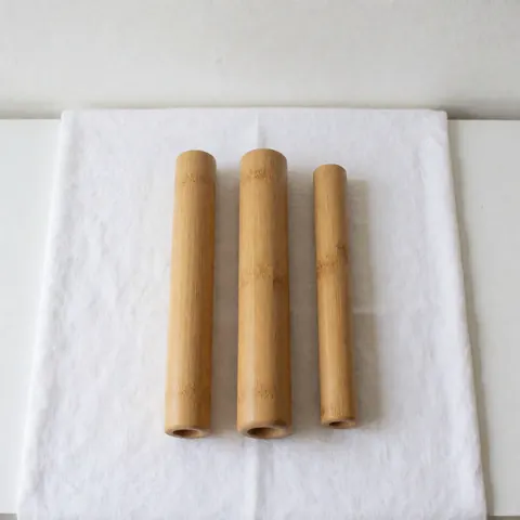 Three clean bamboo Thai massage tubes ready for use, placed on a white textile background for spa and wellness product photography.