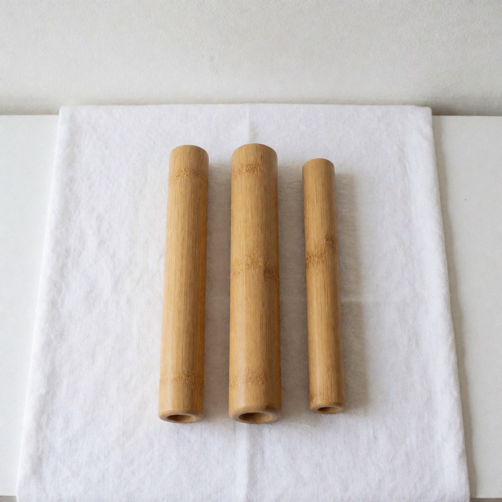 Three clean bamboo Thai massage tubes ready for use, placed on a white textile background for spa and wellness product photography.