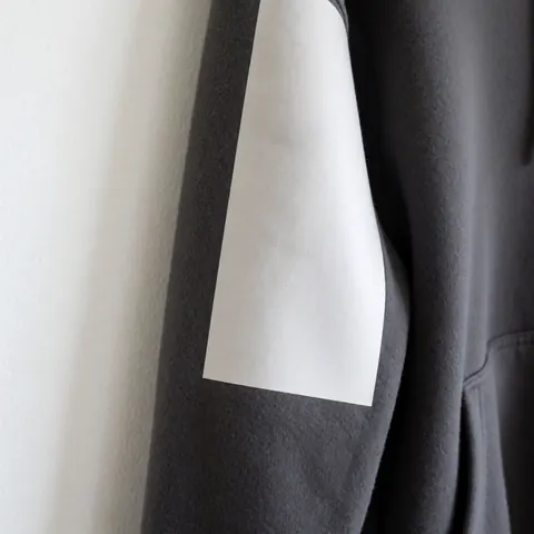 Close-up of a soft matte finish on a gray fleece sweatshirt sleeve with a zipper and pocket against a white wall