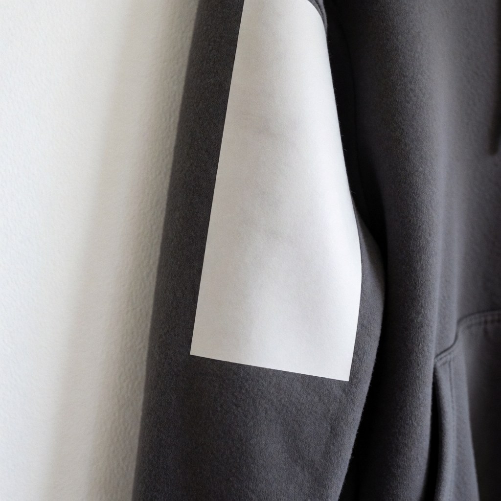 Close-up of a soft matte finish on a gray fleece sweatshirt sleeve with a zipper and pocket against a white wall