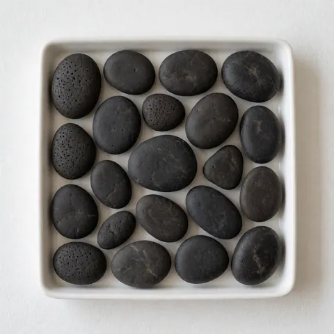 Smooth textured black volcanic rocks arranged on a white plate, suitable for Thai massage and natural wellness treatments