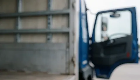 A blurred background view of an industrial loading zone featuring metal structures and a truck door, suitable for logistics and transportation business contexts.