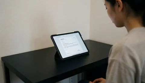 A professional photographer seen from behind working on a tablet at a clean black desk in a minimalist office setting with soft lighting