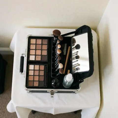 Open professional makeup kit on white table with eyeshadow palette, brushes, mirror, and setting spray ready for client service