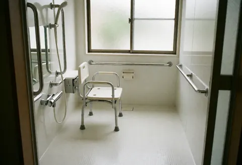 Clean accessible bathroom interior featuring a white shower chair, chrome grab bars, and non-slip flooring for geriatric care and rehabilitation therapy.