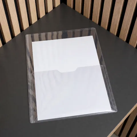 Clear plastic document sleeve with front window resting on a black table, ideal for presenting theses or reports against a light wood slat background.