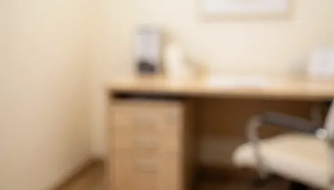 Soft focus clinical office with desk, filing cabinet, and chair in warm beige tones, ideal for hypnotherapy text overlays