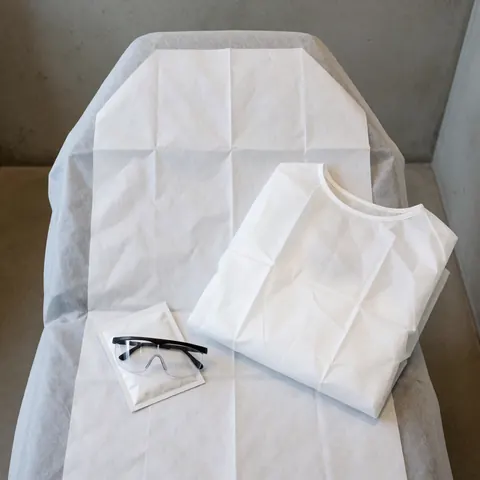 Clean treatment bed with disposable towel, protective clothing, and safety glasses ready for laser hair removal in a professional clinic.