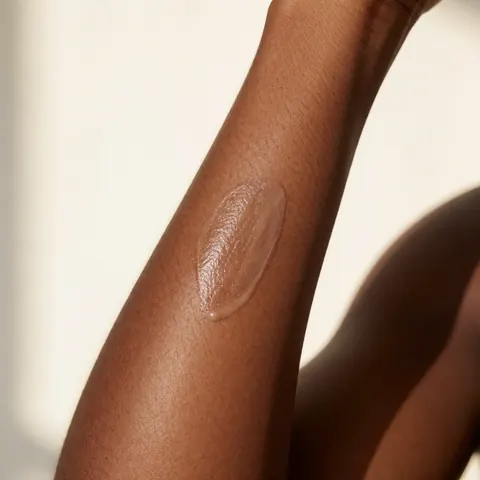 Close-up of a smooth, hairless arm with a small amount of hydrating product applied, featuring warm lighting and a neutral background.