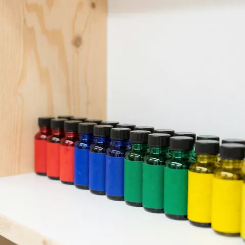 Rows of vibrant vegan ink bottles on a white shelf with a light wood background, suitable for tattoo studio product display
