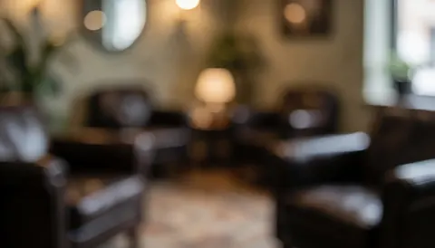 Soft focus background of a tattoo studio waiting area featuring dark leather chairs, warm lighting, and wooden walls, perfect for text overlays.