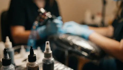 Warmly lit tattoo studio workspace featuring ink bottles, a razor, and blue gloves on a blurred background, ideal for text overlay.