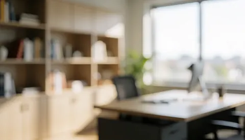 Blurred modern office interior featuring shelves, a desk, and windows with warm soft lighting, ideal for business text overlays