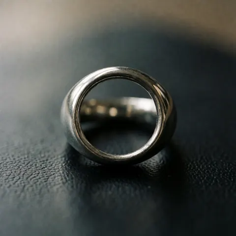 Polished metal ring with reflections on textured black leather surface with dramatic lighting and blurred background