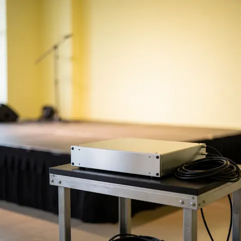 Silver professional audio equipment on a metal table with coiled cable, set against a yellow wall with a blurred background.