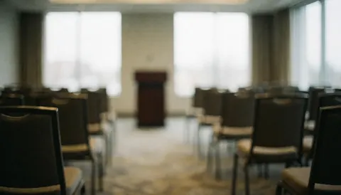 Out of focus conference room with rows of chairs and a podium in the background, natural light from windows, suitable for corporate text overlays