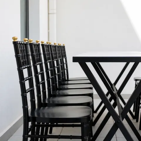Black chairs with gold accents lined up next to a modern table in a minimalist outdoor patio with white walls