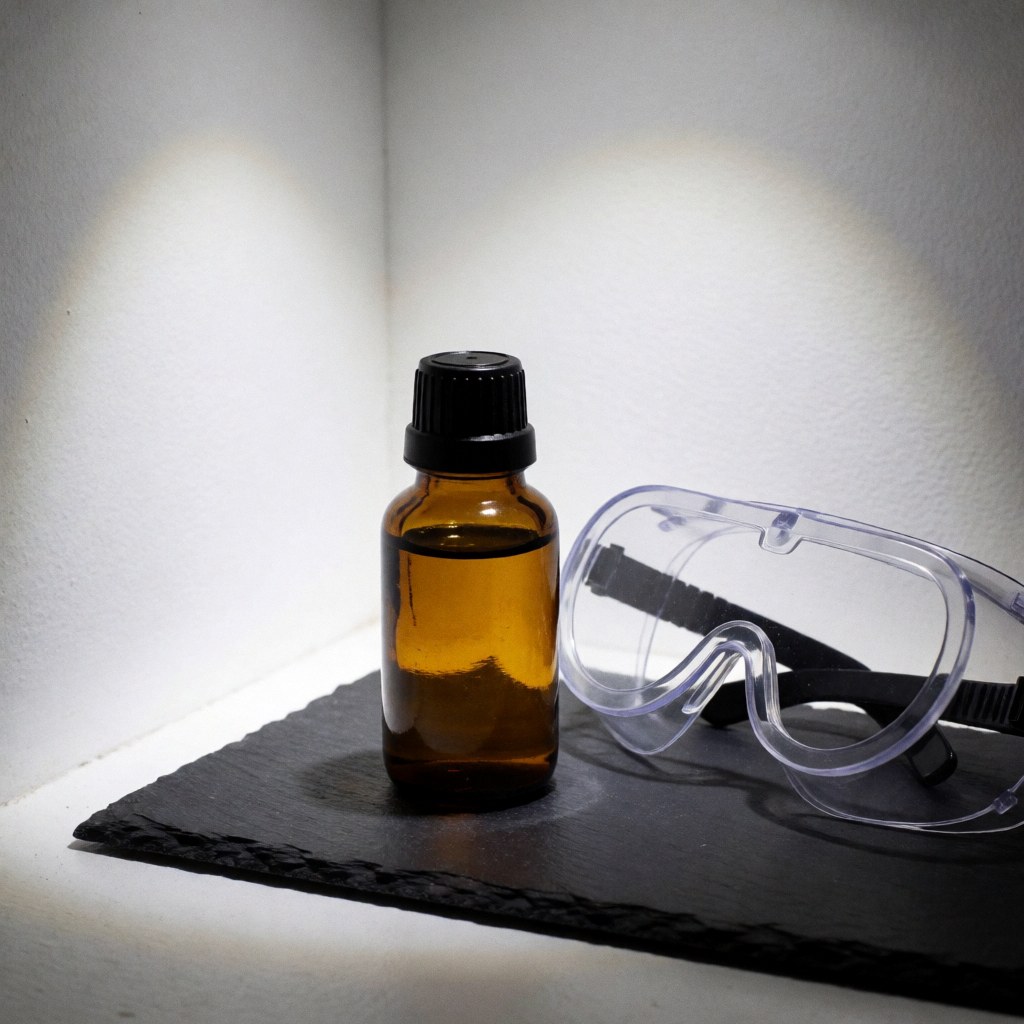 Amber glass bottle with black cap and clear safety goggles on black slate, dramatic lighting in white corner
