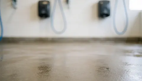 Wet concrete floor in a car wash with blurred soap dispensers on the wall, soft neutral lighting ideal for text overlay